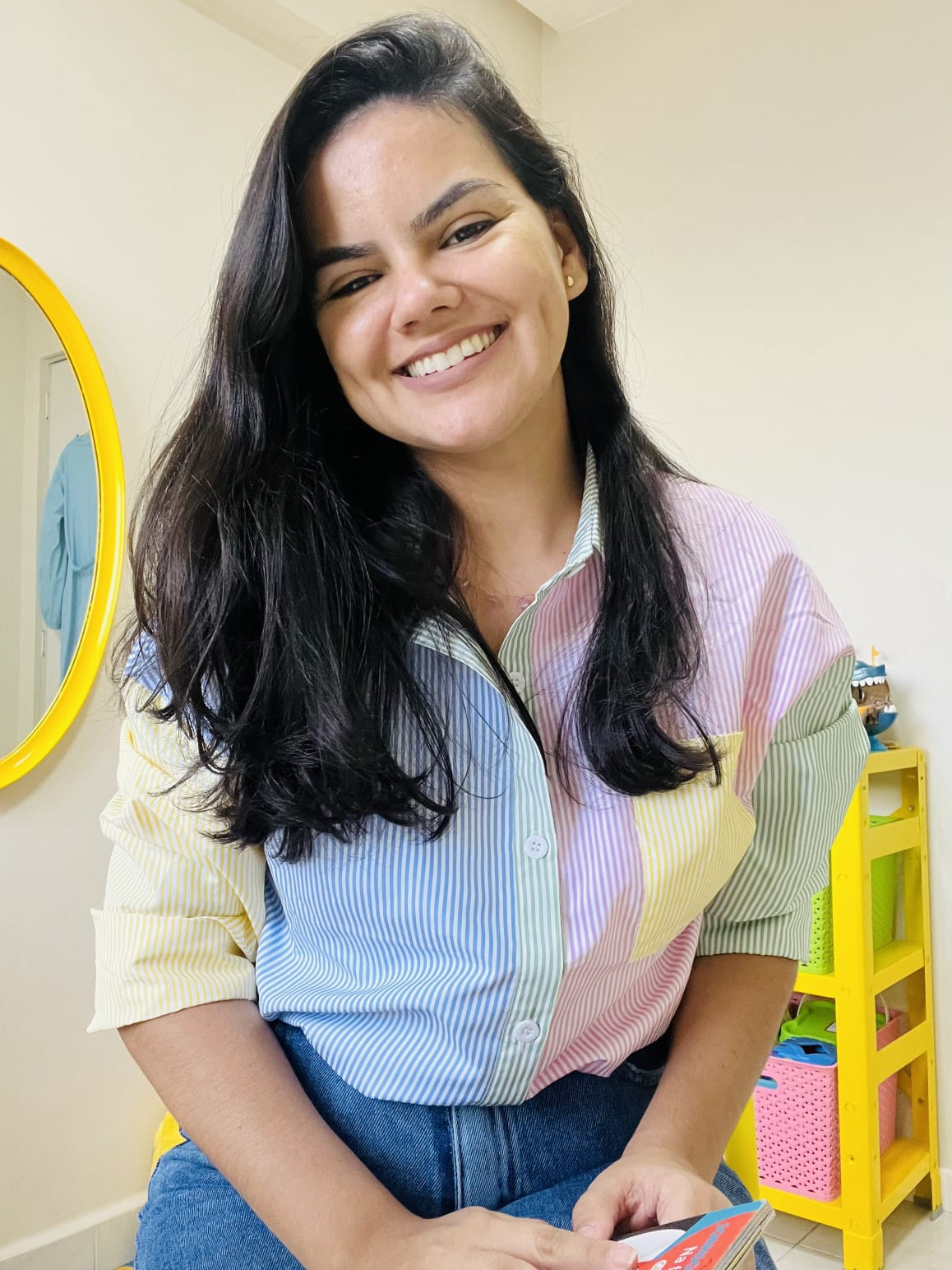 Denise Mota, fonoaudióloga infantil, sorrindo em consultório com decoração lúdica